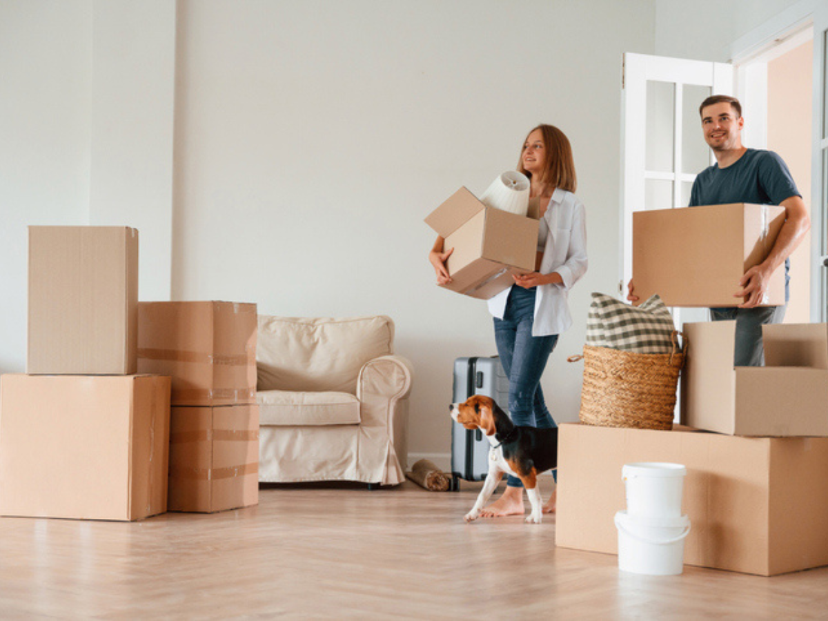 A smiling couple moving boxes into their new home while considering the average house insurance cost in BC.