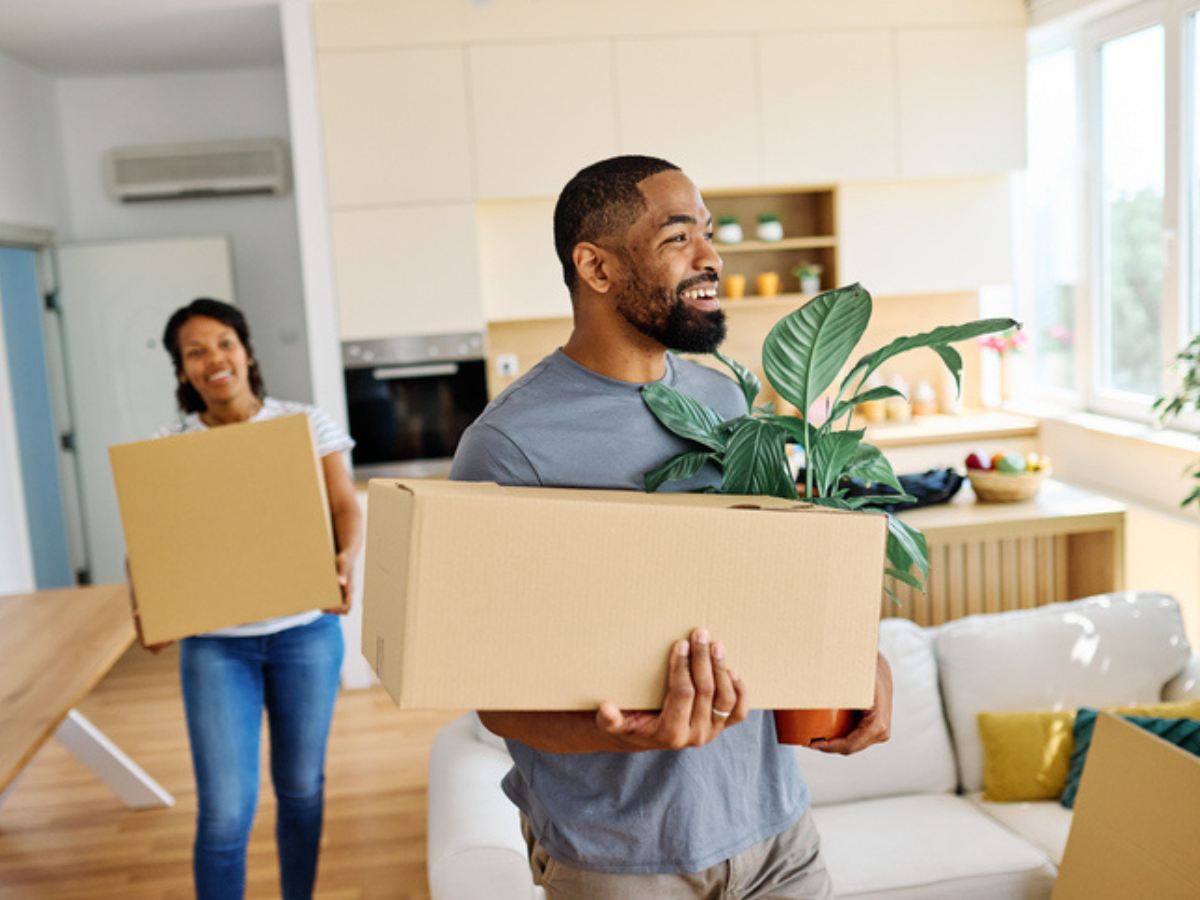 A smiling couple moving boxes into their new home while considering the average house insurance cost in BC.