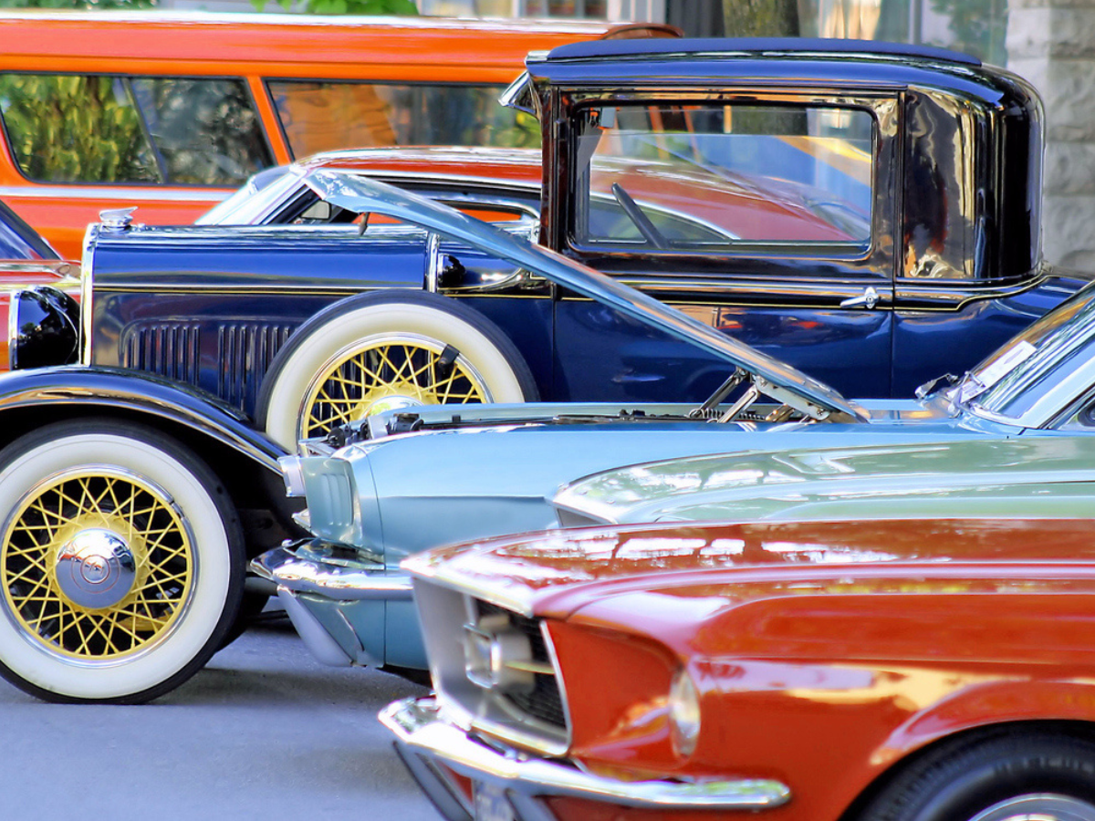 Row of restoared classic care as prked outdoors with hoods open, showcasing vintage vehicle condition for insurancnd appraisal