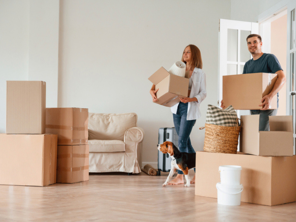 People carrying boxes into a new rental home surrounded by packed belongings and household items