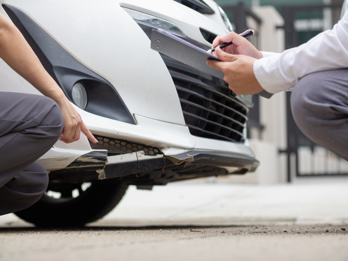 Damaged front bumper being inspected and documented after a vehicle collision.