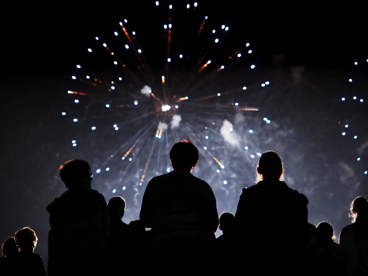 Crowd watching a bright Firework display illuminate the night sky.