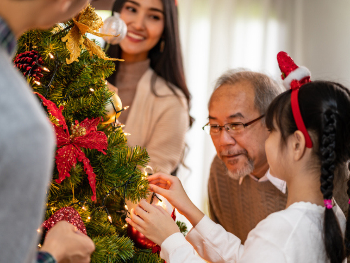Family decorating a Christmas tree with ornaments and lights during the holiday season.