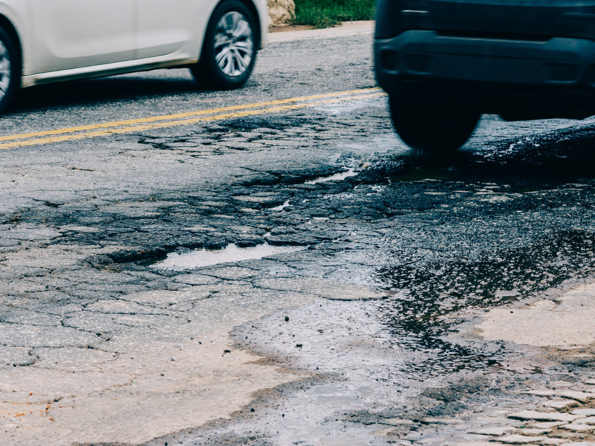 Rain-filled potholes on a damaged road as vehicles pass by