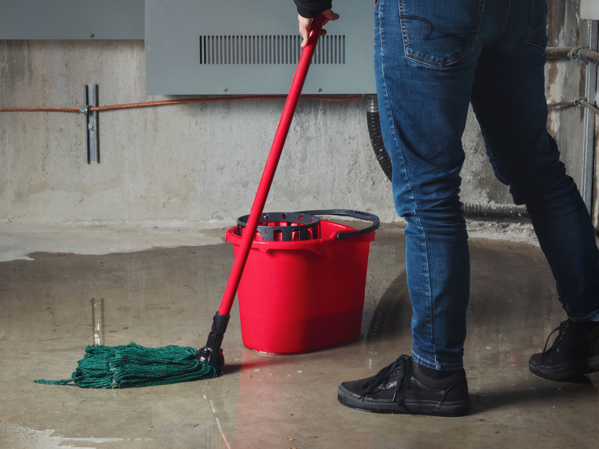 Person mopping a flooded basement floor after Water Damage caused by a plumbing or drainage issue