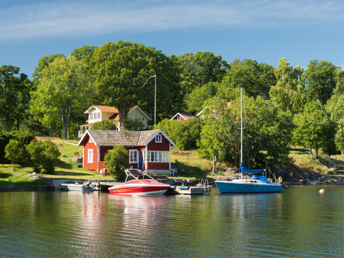 Cabin at a Seasonal Property by the waterfront with boats docked and lush trees on a sunny day.