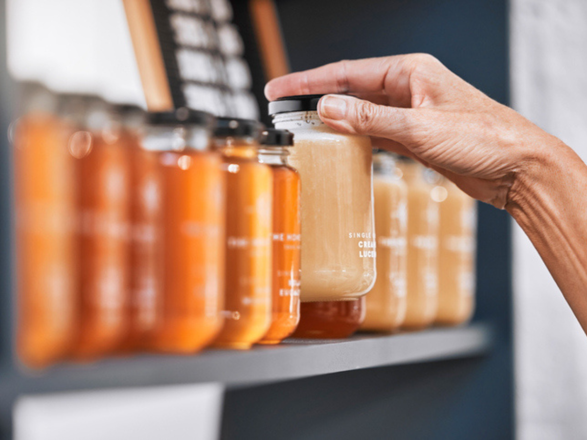 Hand reaching for a jar of honey among rows of honey jars on a shop shelf