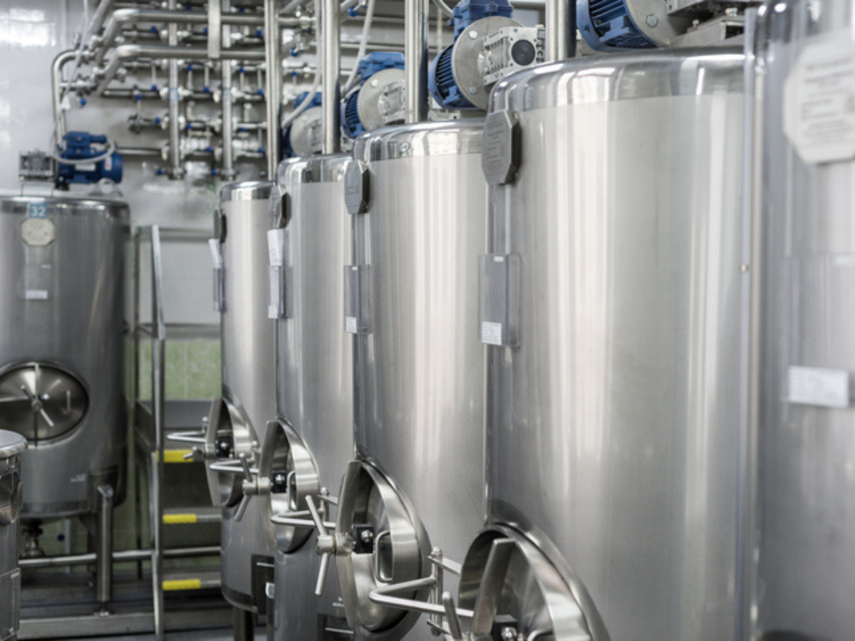 Row of large stainless steel storage tanks and piping inside a dairy processing facility