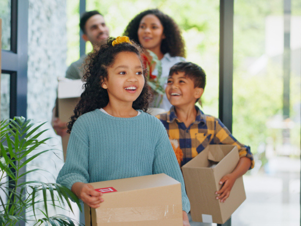 A family walks in together to their new home, carrying boxes with them.