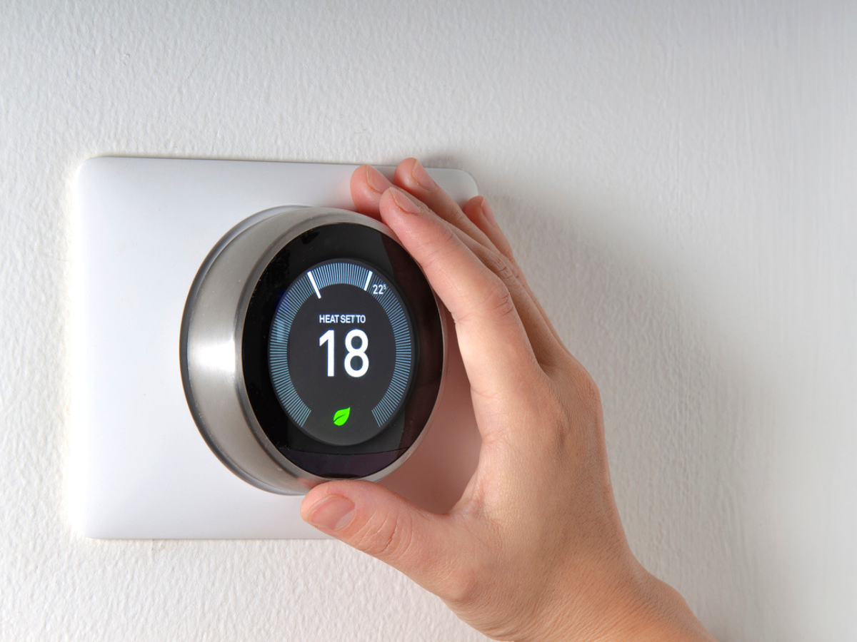 Hand adjusting a smart thermostat mounted on an interior wall.