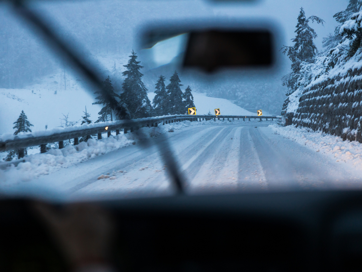 View through a windshield of a snow-covered mountain road during winter driving.
