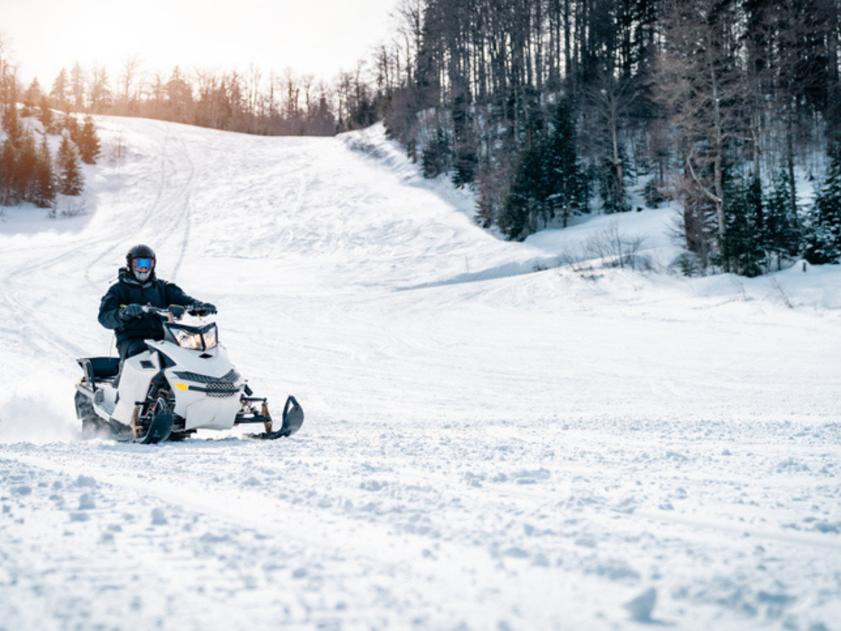 Snowmobile moving through a snowy landscape surrounded by trees and open terrain.