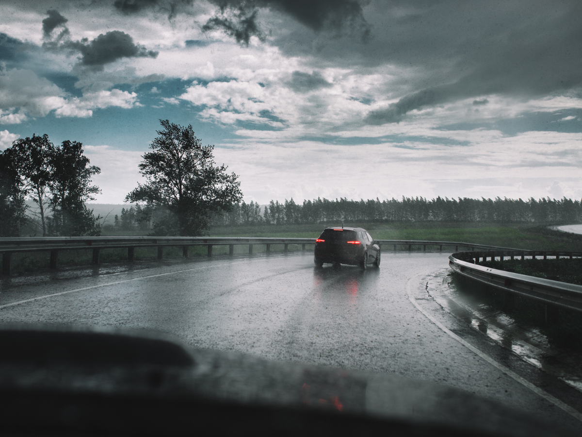 Car navigating a curved highway during heavy Rain under dark storm clouds