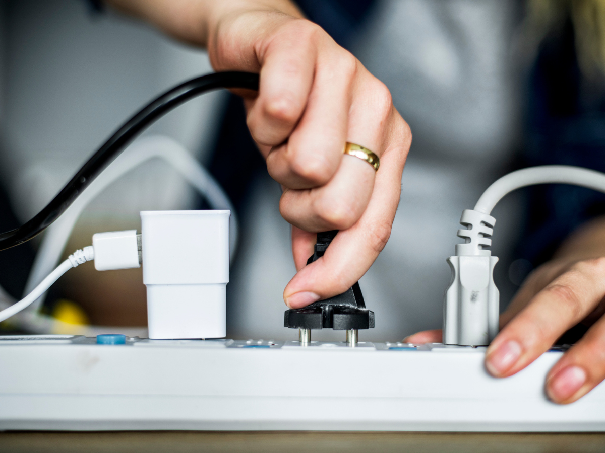 Hand connecting an electrical plug to a power strip with several cords attached