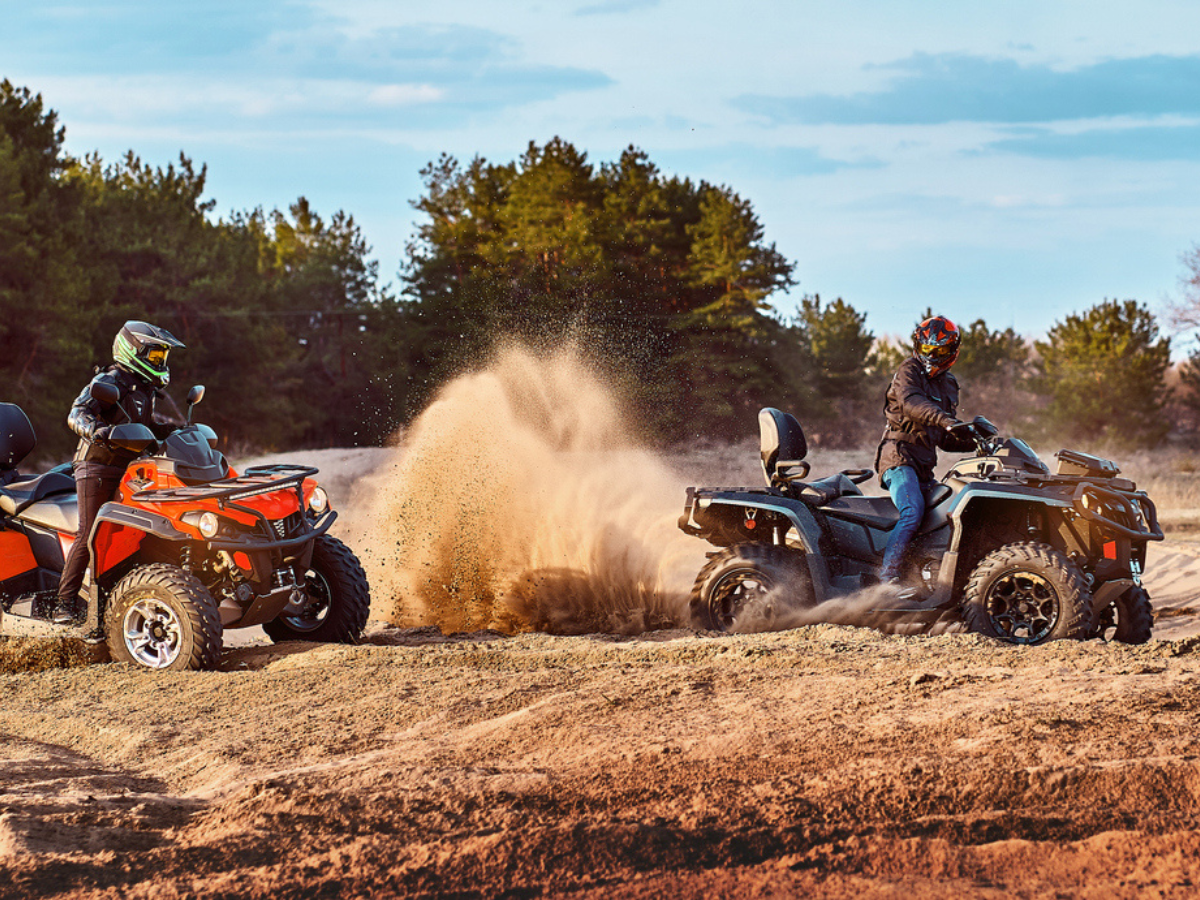 Two ATV riders kicking up dust on a sandy off-road trail during an adventure.