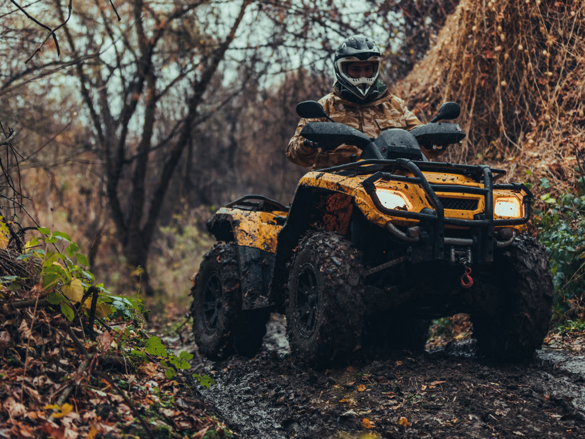 Rider operating an ATV through a muddy forest trail, demonstrating off-road performance and traction