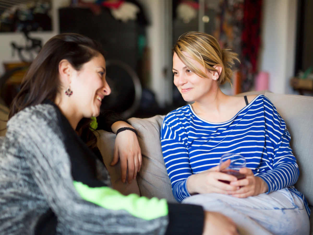 Two people chatting in a living room while seated on a sofa.