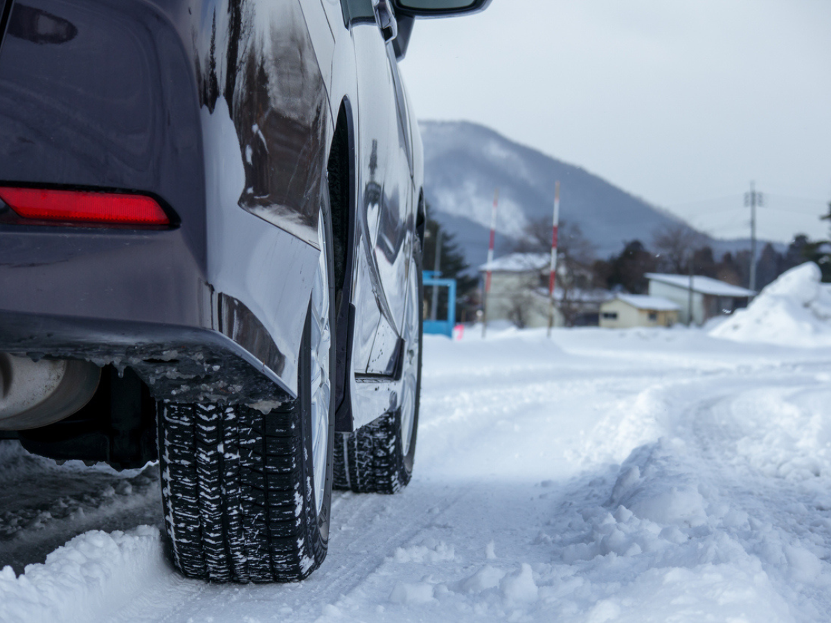 Vehicle equipped with winter tires parked on a snowy roadway near a mountain landscape.