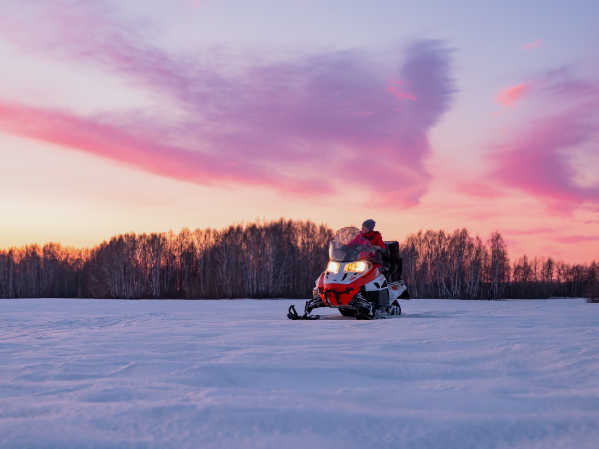 Snowmobile parked on a snowy field beneath a colorful winter sunset sky.