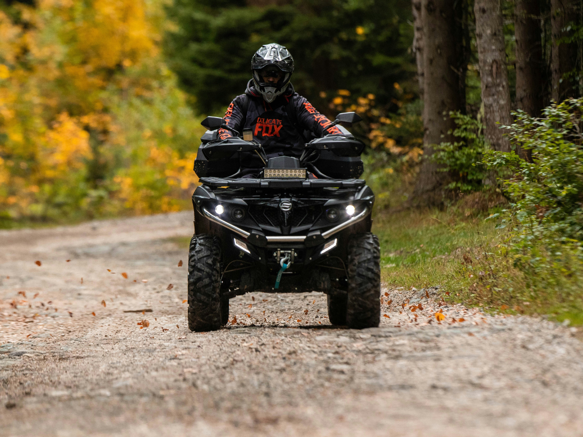Solo ATV rider driving through an autumn forest on a gravel trail protected by Sandbox ATV coverage.