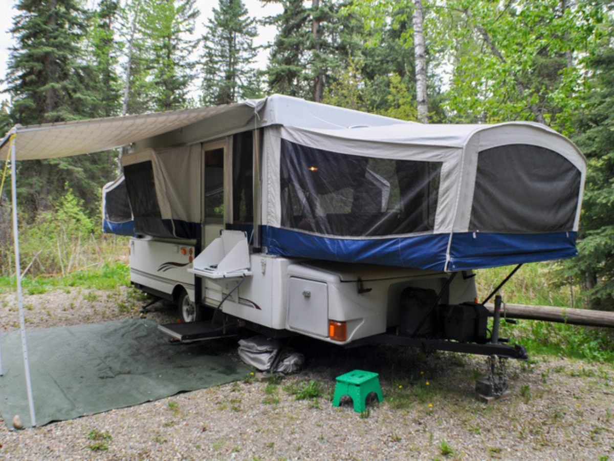 Pop-up tent trailer set up with awning at a forested campsite