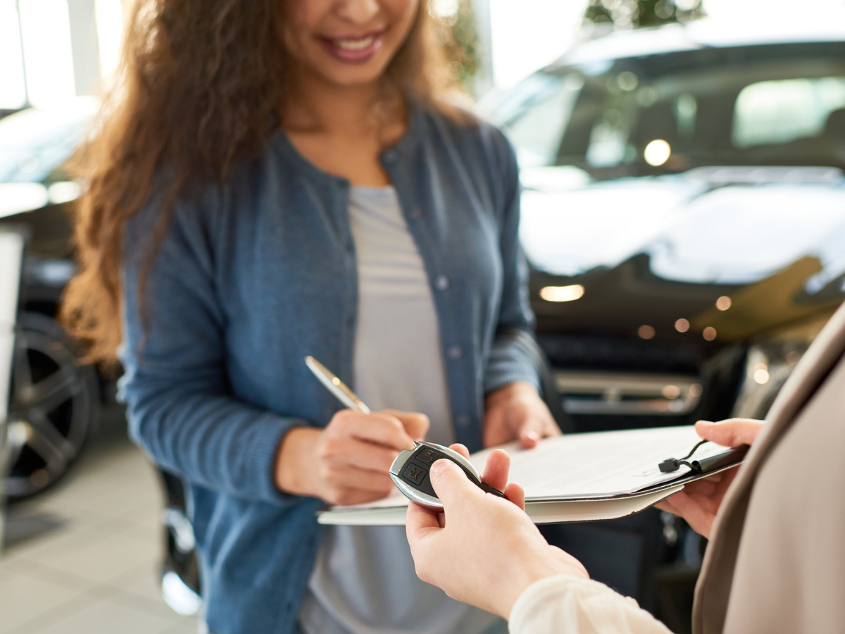 Customer signing paperwork while receiving car keys at a vehicle dealership.
