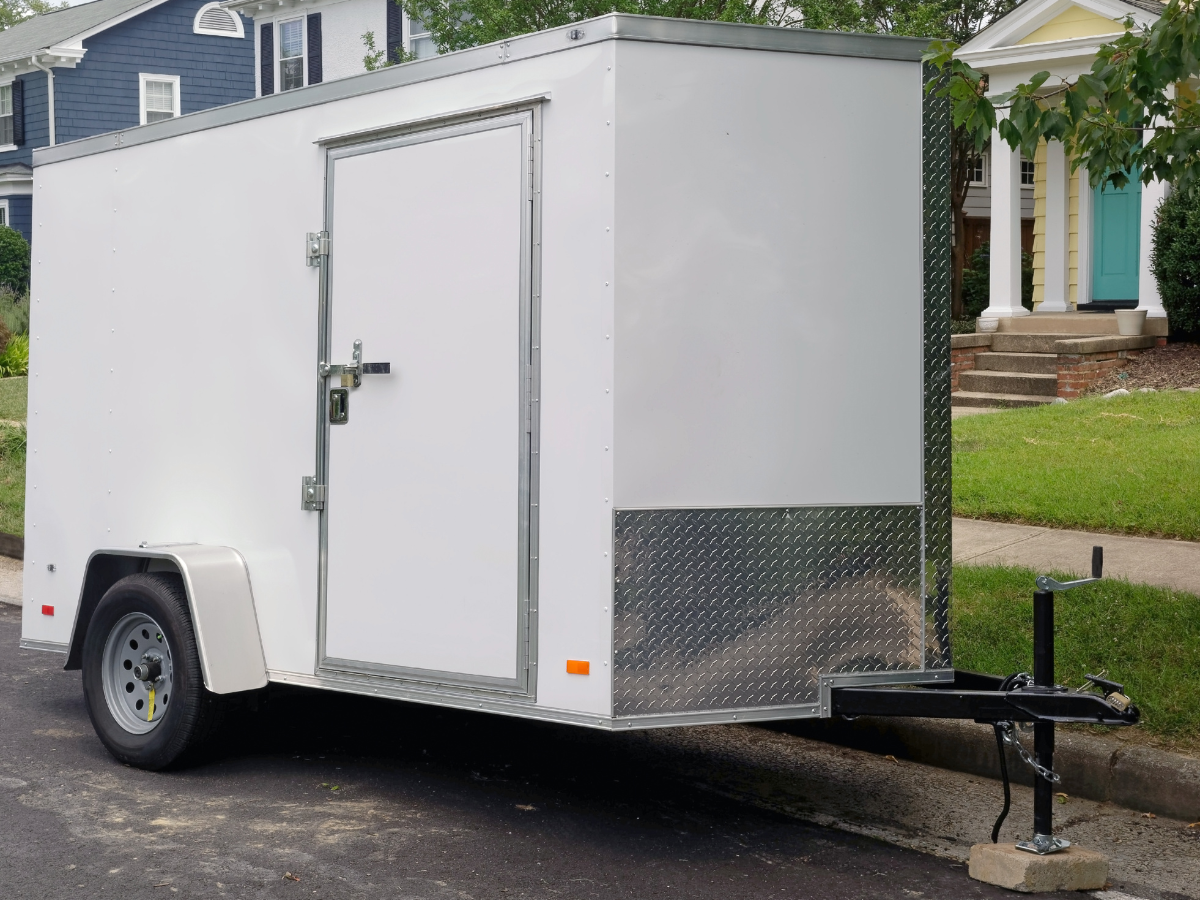 A large white enclosed cargo trailer parked on a residential street, showcasing valuable gear protected under a comprehensive policy.