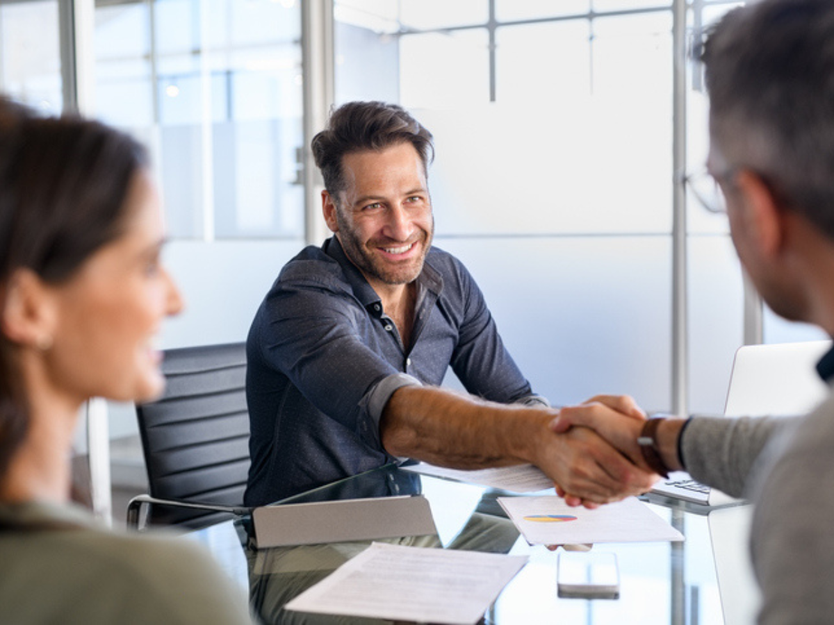 Business owner meeting with insurance broker and shaking hands, representing the importance of reviewing business insurance coverage regularly.