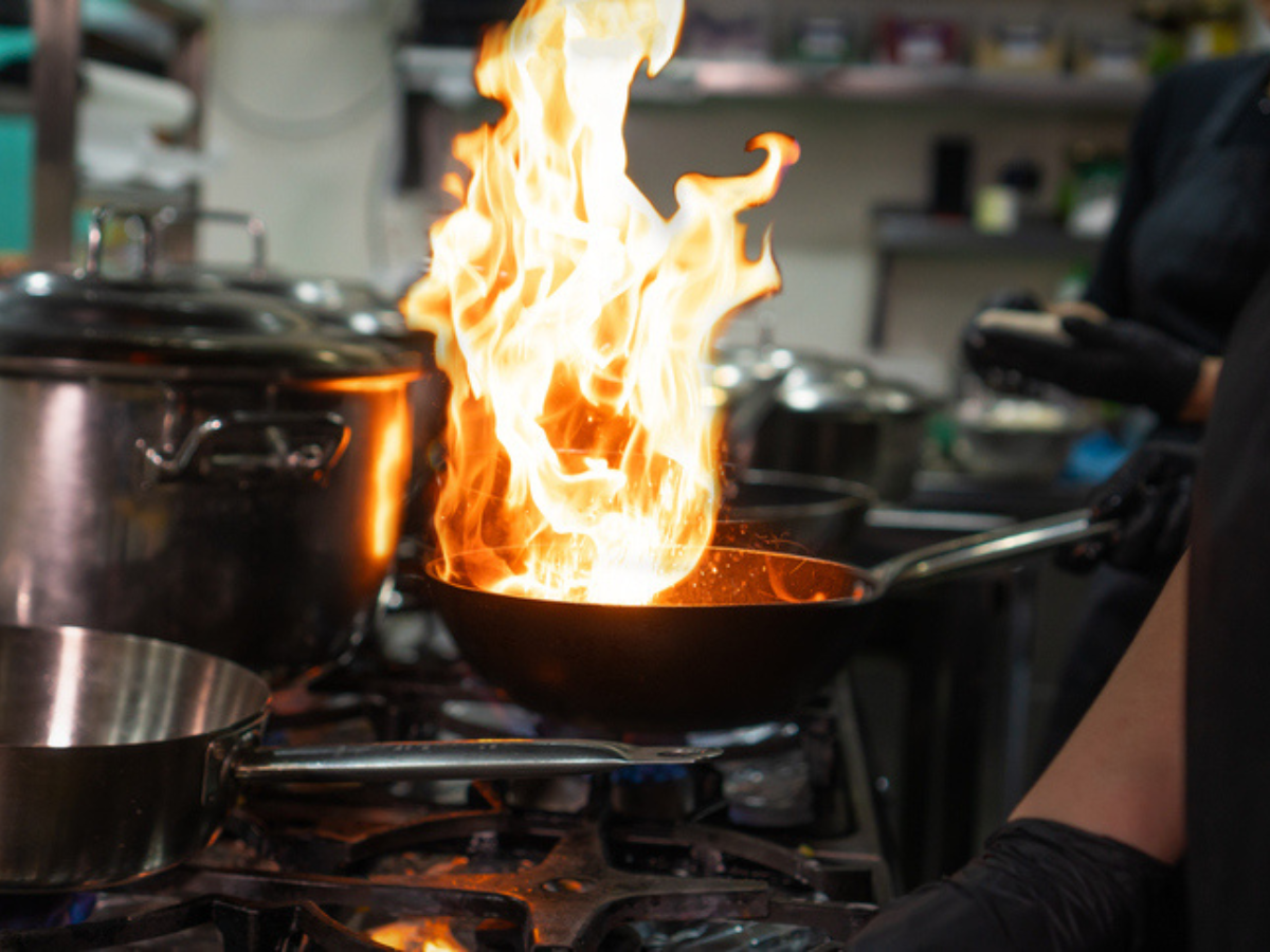Flames rise from a frying pan on a commercial kitchen stove, highlighting fire risks faced by restaurants and the importance of having comprehensive restaurant insurance coverage.