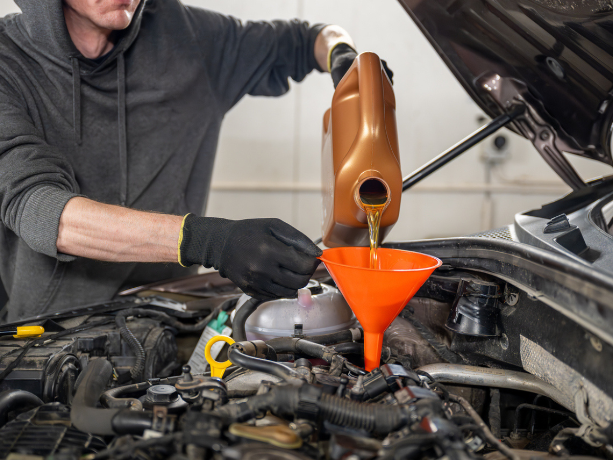Person pouring motor oil into a car engine, representing routine maintenance for vintage vehicles and the importance of protecting them with classic car insurance.