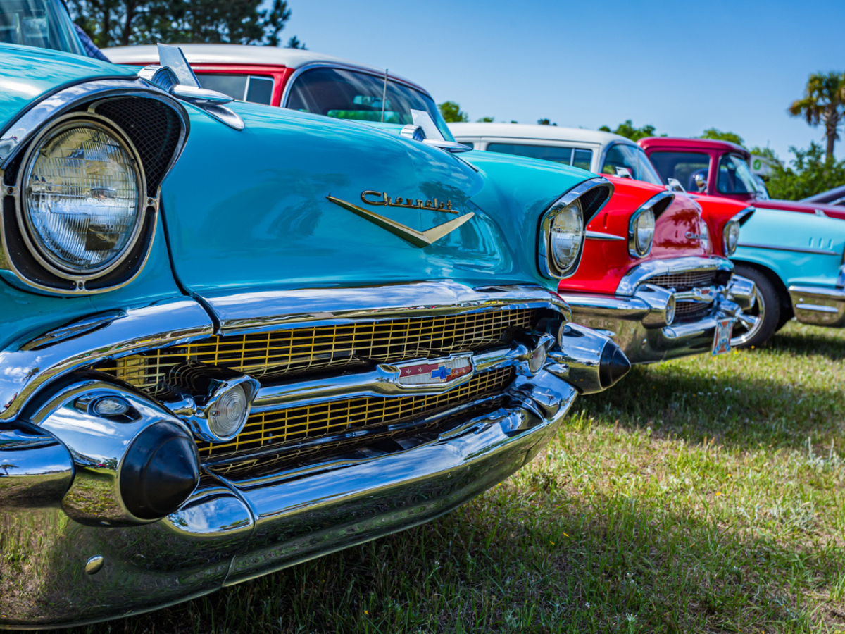 Lineup of brightly colored vintage cars at a classic car show, highlighting the pride of ownership and the value of protecting these timeless vehicles with classic car insurance.