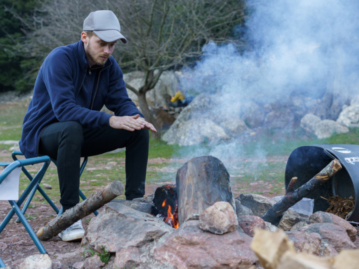 A man attentively monitors a campfire while warming his hands, illustrating responsible fire pit use and the importance of staying present to help prevent outdoor fire hazards.
