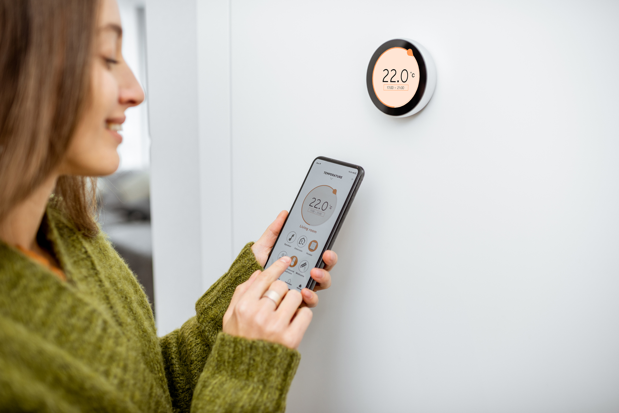 A women adjusts the temperature in her home with a smart thermostat