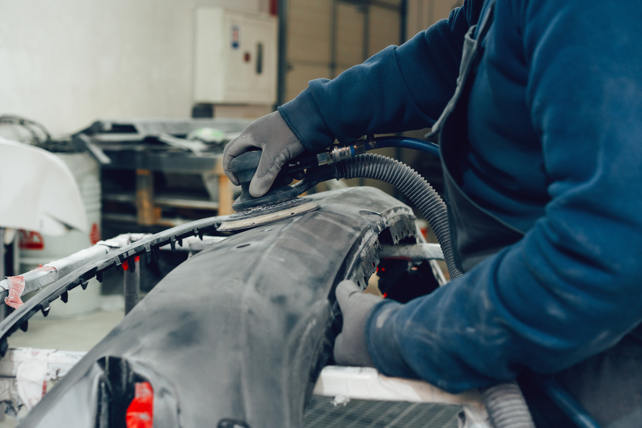 Technician sanding a car panel in an auto body shop during vehicle restoration process, highlighting repair work for insurance coverage”