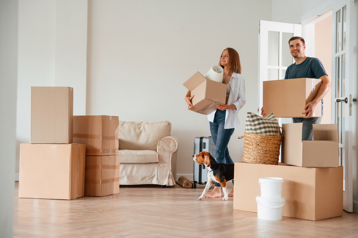 Couple moving into new apartment with moving boxes and dog, highlighting renter coverage, tenant insurance protection, and apartment insurance for personal belongings during relocation.