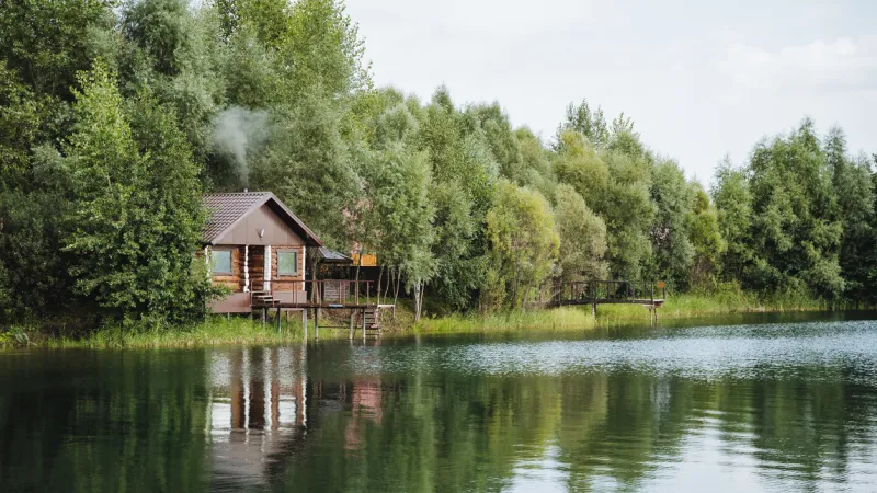 Lake house in a forest reflecting on water.