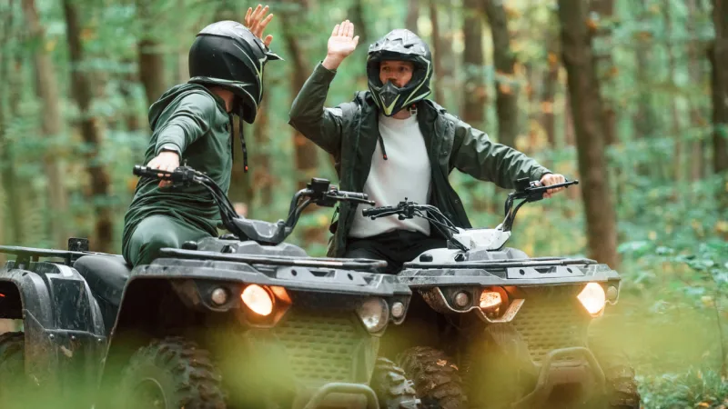 Two riders having fun and high-fiving on a trail, knowing they are protected by Sandbox ATV insurance coverage.