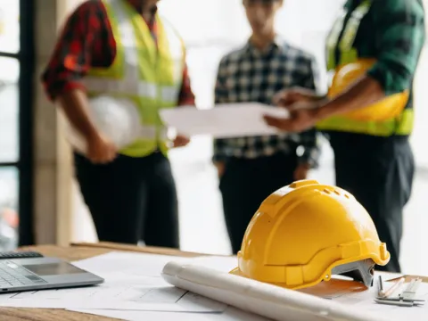 Contractors reviewing building plans while a hard hat and laptop sit on a work table