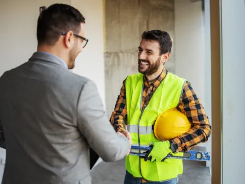 Contractor and project manager shaking hands on a job site while discussing construction plans.