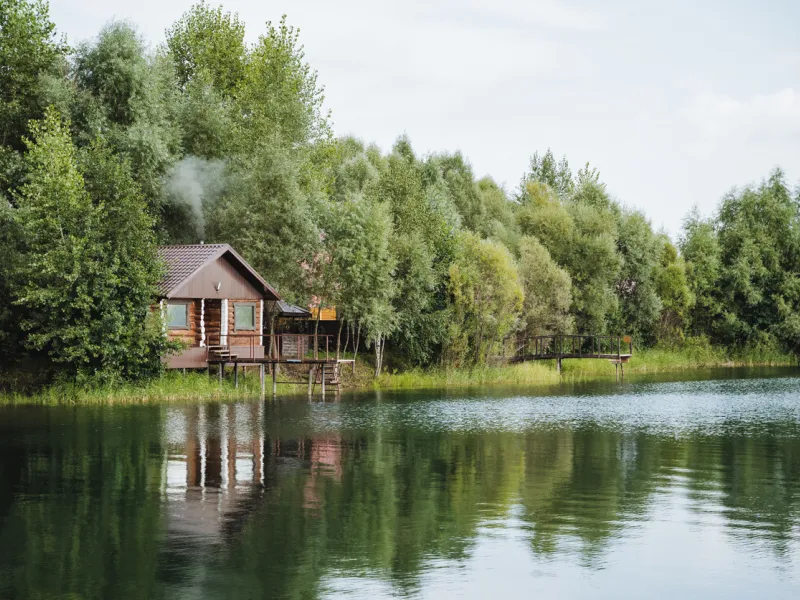 Lake house in a forest reflecting on water.