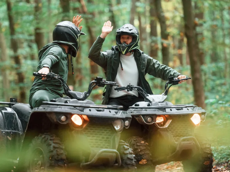 Two riders having fun and high-fiving on a trail, knowing they are protected by Sandbox ATV insurance coverage.