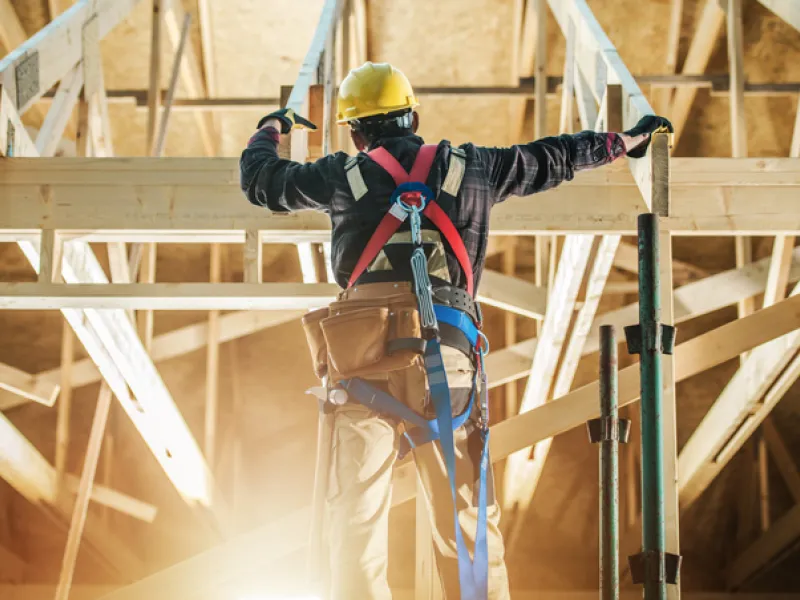 A construction worker wearing safety gear installing roof trusses on a building site protected by builders risk insurance